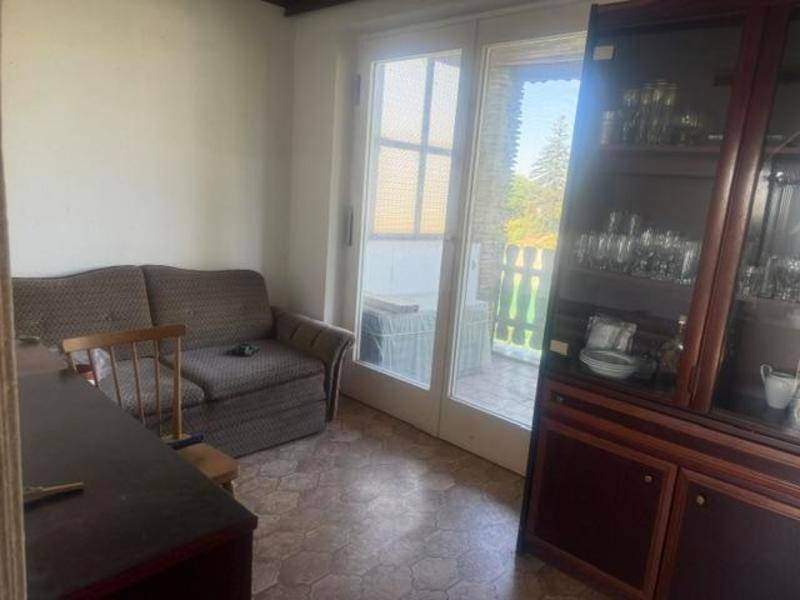 Wohnzimmer mit Sofa, Vitrinenschrank und Zugang zu einem Außenbereich durch eine Glastür.