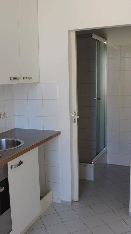 Kleine Küchenzeile mit weißen Schränken und angrenzender Duschkabine.