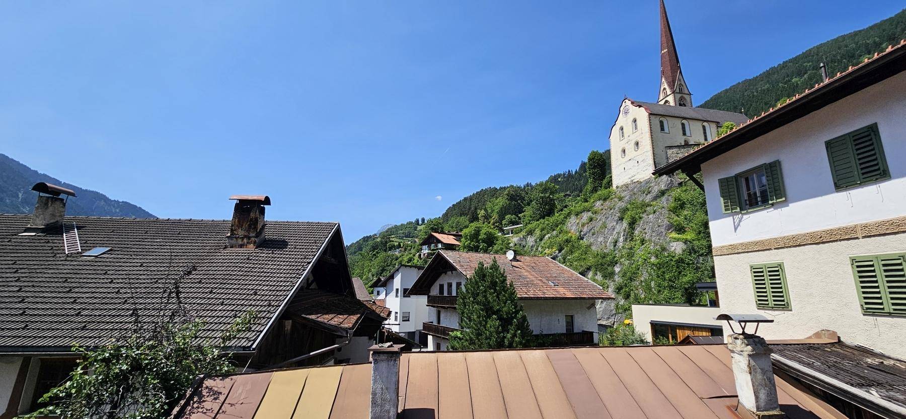 Panoramablick auf die alpine Landschaft mit traditionellen Häusern und einer Kirche auf dem Hügel.