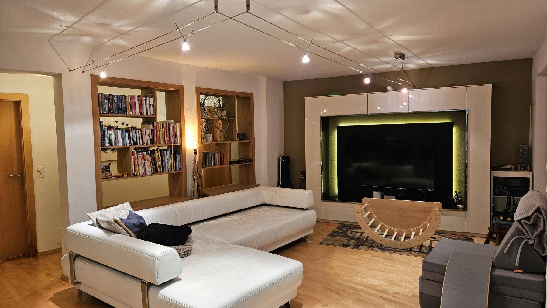 Gemütlicher Wohnbereich mit großem Fernseher, weißem Sofa und integrierten Holzregalen.
