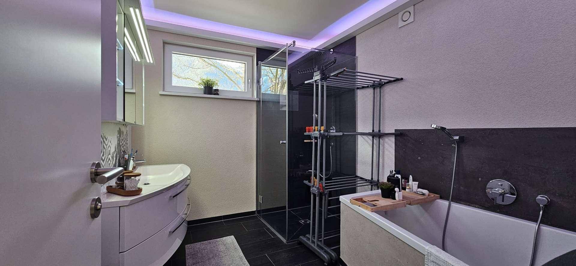Modernes Badezimmer mit Badewanne, Duschkabine und Fenster für angenehmes Tageslicht.
