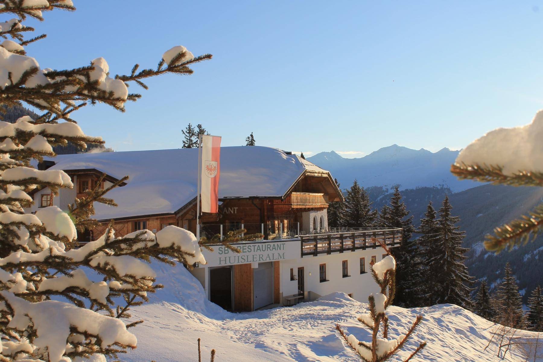 Idyllisches Berghaus im Winter, umrahmt von schneebedeckten Ästen und einer malerischen Bergkulisse im Hintergrund.