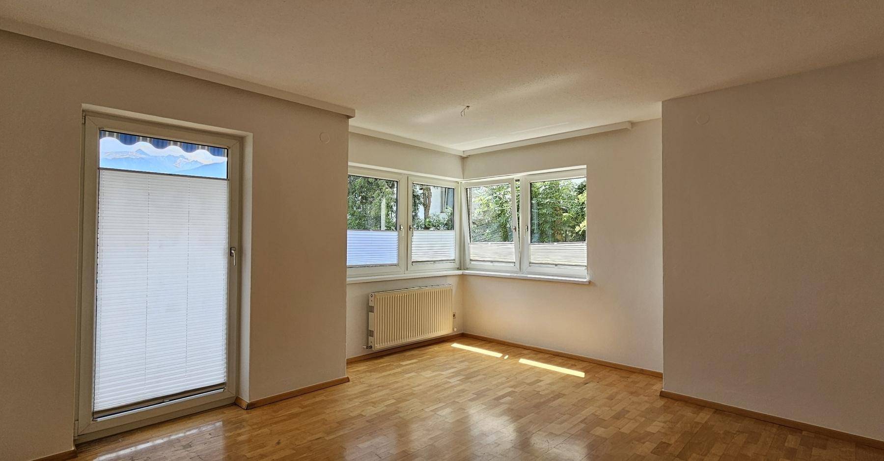 Helles Zimmer mit Parkettboden und großen Fenstern, die viel Tageslicht hereinlassen und einen Zugang nach draußen bieten.
