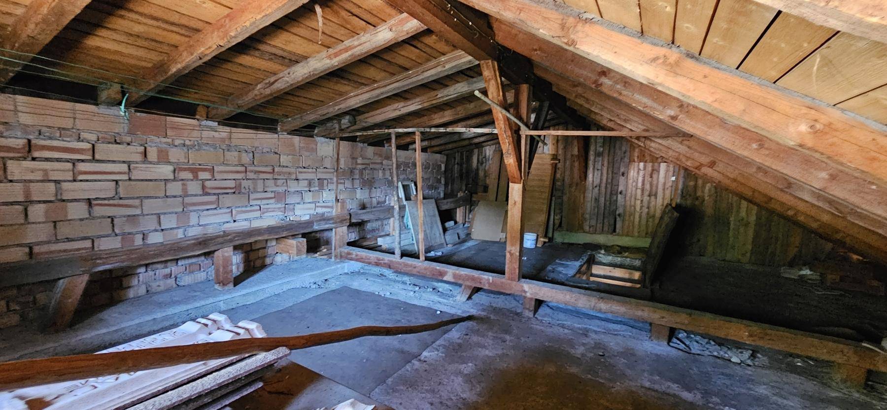 Unausgebauter Dachboden mit sichtbaren Holzbalken und Ziegelwänden, ideal für einen Ausbau.