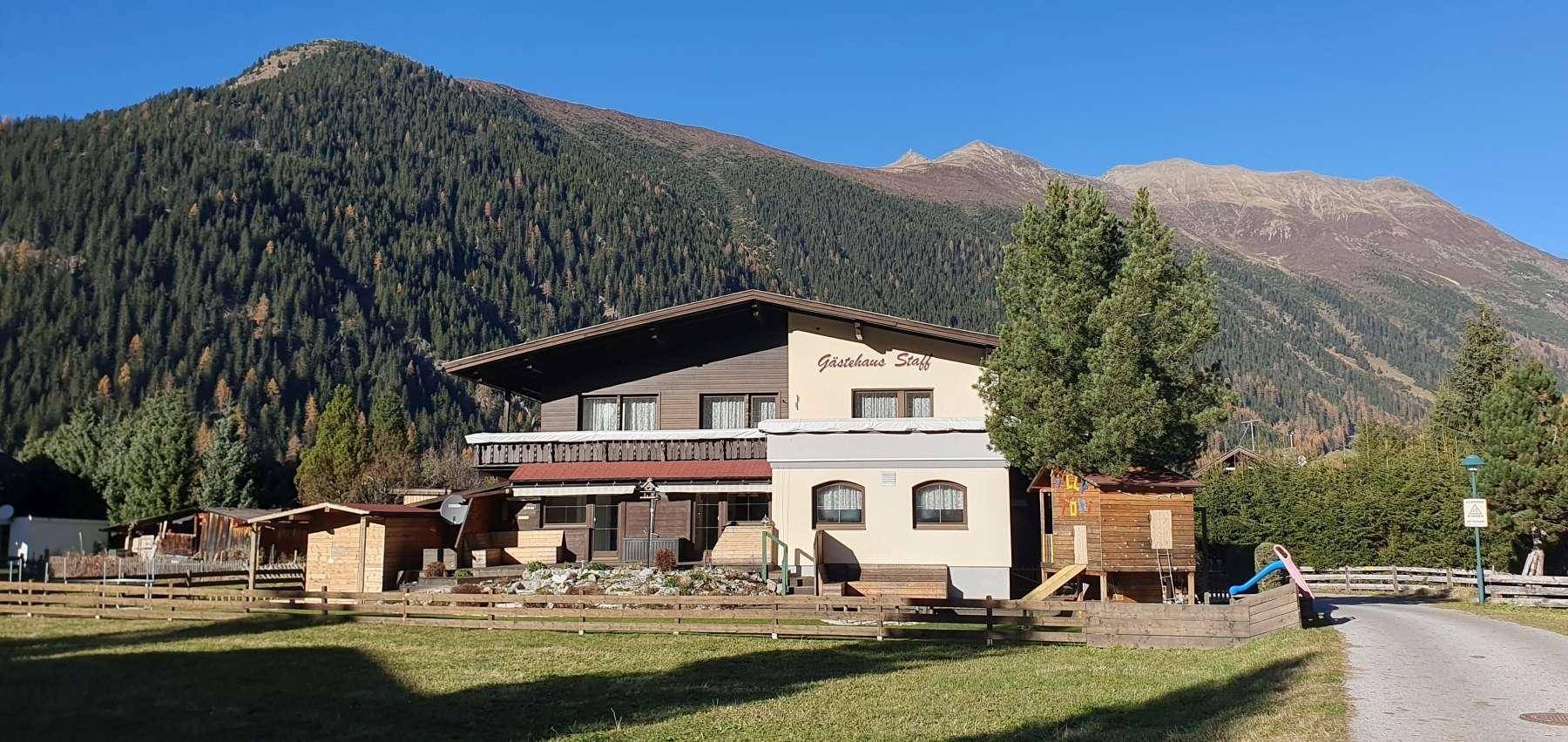 Gasthaus in den Bergen mit Spielplatz im Vordergrund, umgeben von grünen Wiesen und Wäldern.