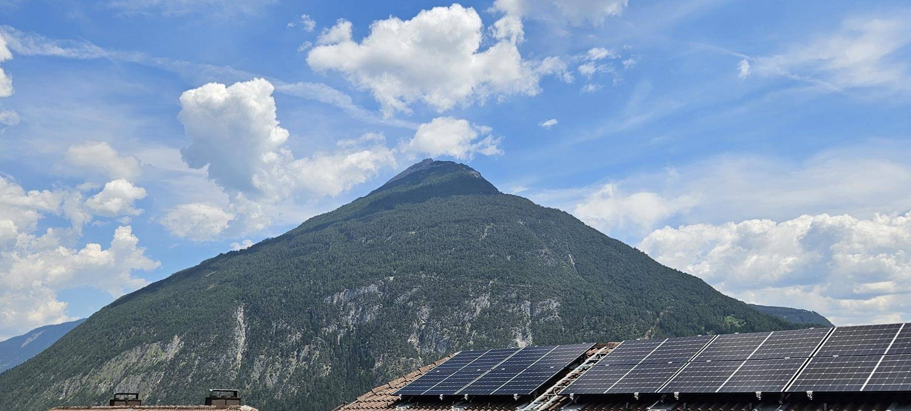 Beeindruckender Bergblick über Dächer mit installierten Photovoltaik-Modulen unter blauem Himmel.