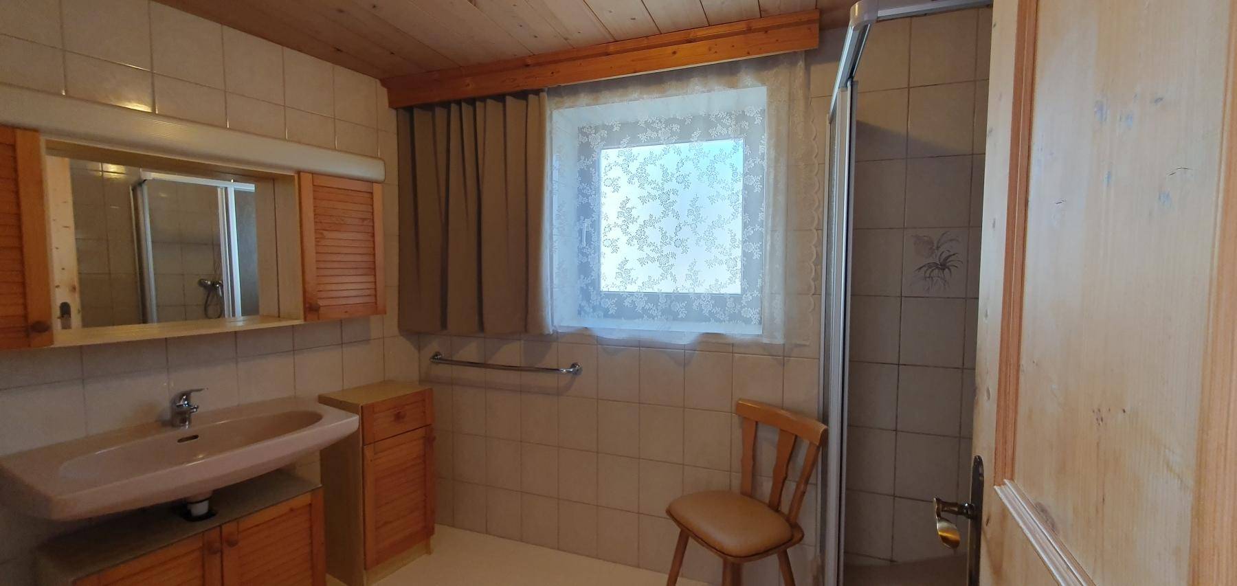 Badezimmer mit Dusche, Fenster und hellen Fliesen an den Wänden.
