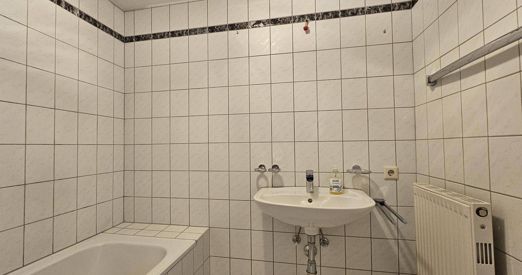 Gefliestes Badezimmer mit Badewanne und Waschbecken, ausgestattet mit einem Heizkörper.