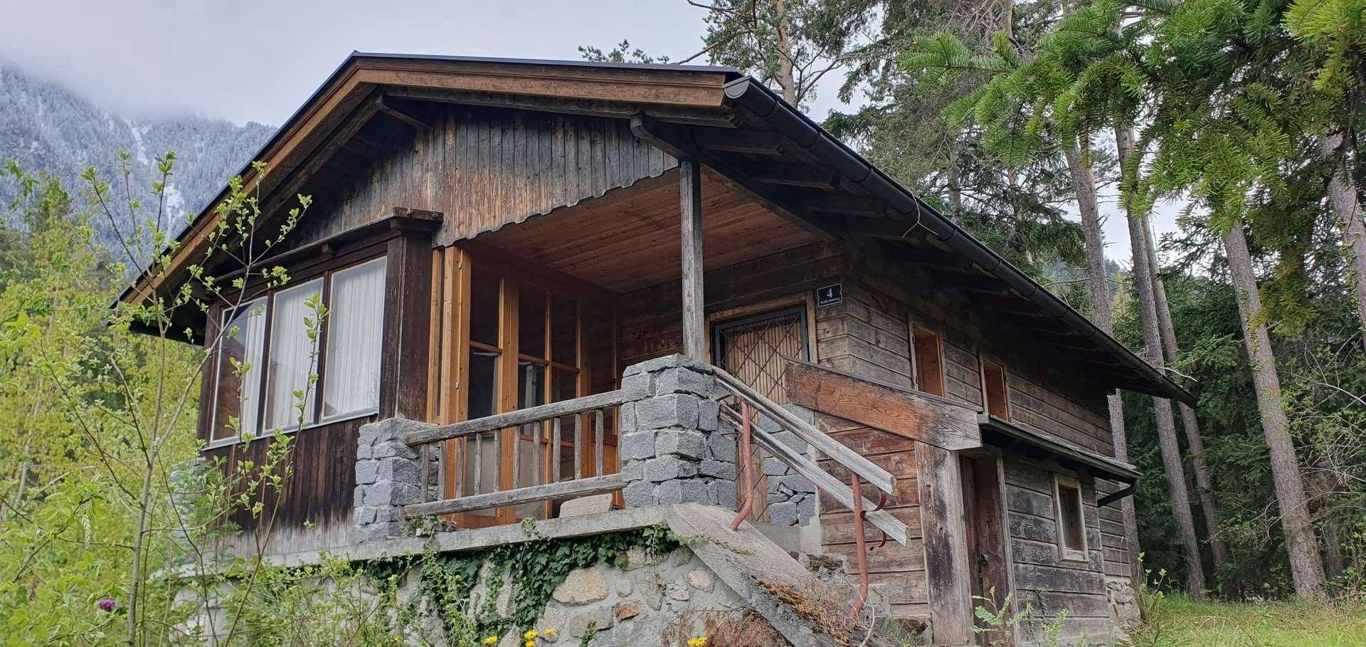 Detailansicht des rustikalen Holzhauses mit Steinfundament und überdachtem Eingangsbereich.