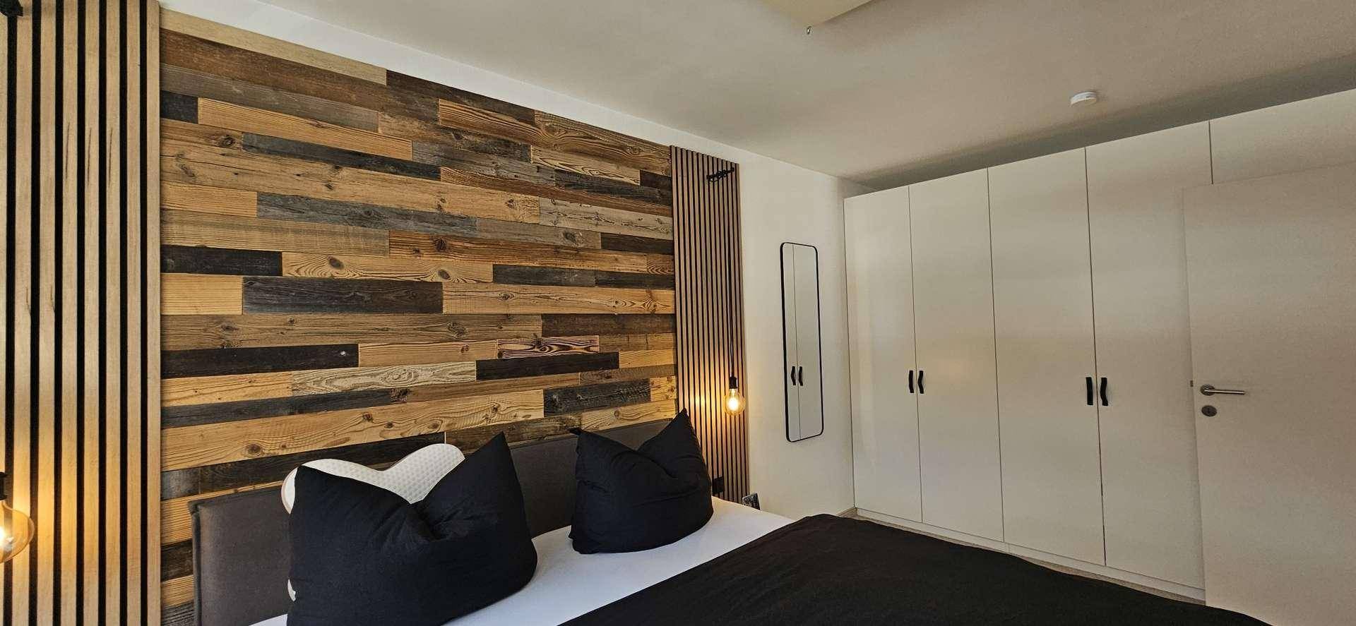 Schlafzimmer mit Holzakzentwand, integrierten Einbauschränken und minimalistischer Einrichtung.