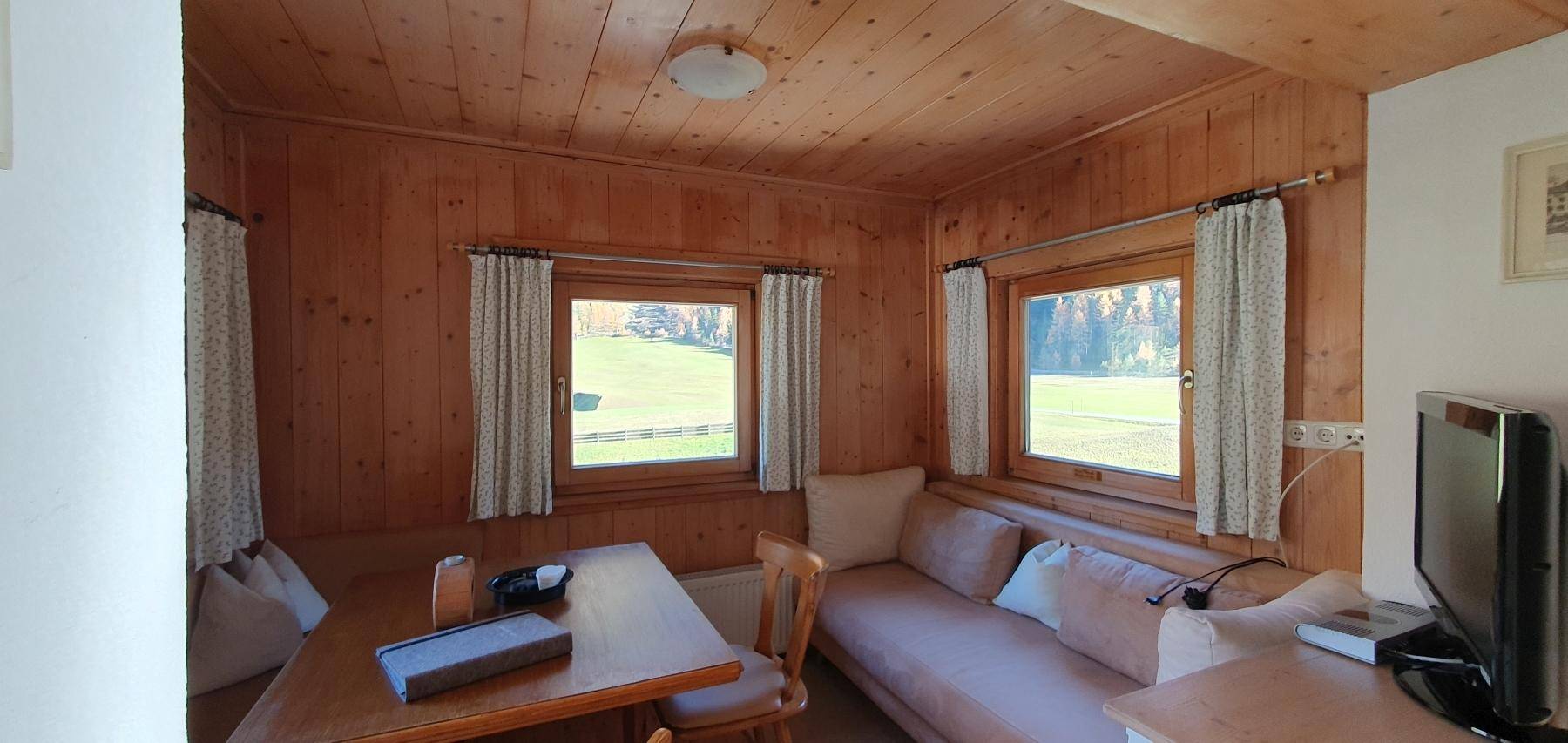 Gemütlicher Wohnbereich mit Holztäfelung und Blick ins Grüne durch die Fenster.