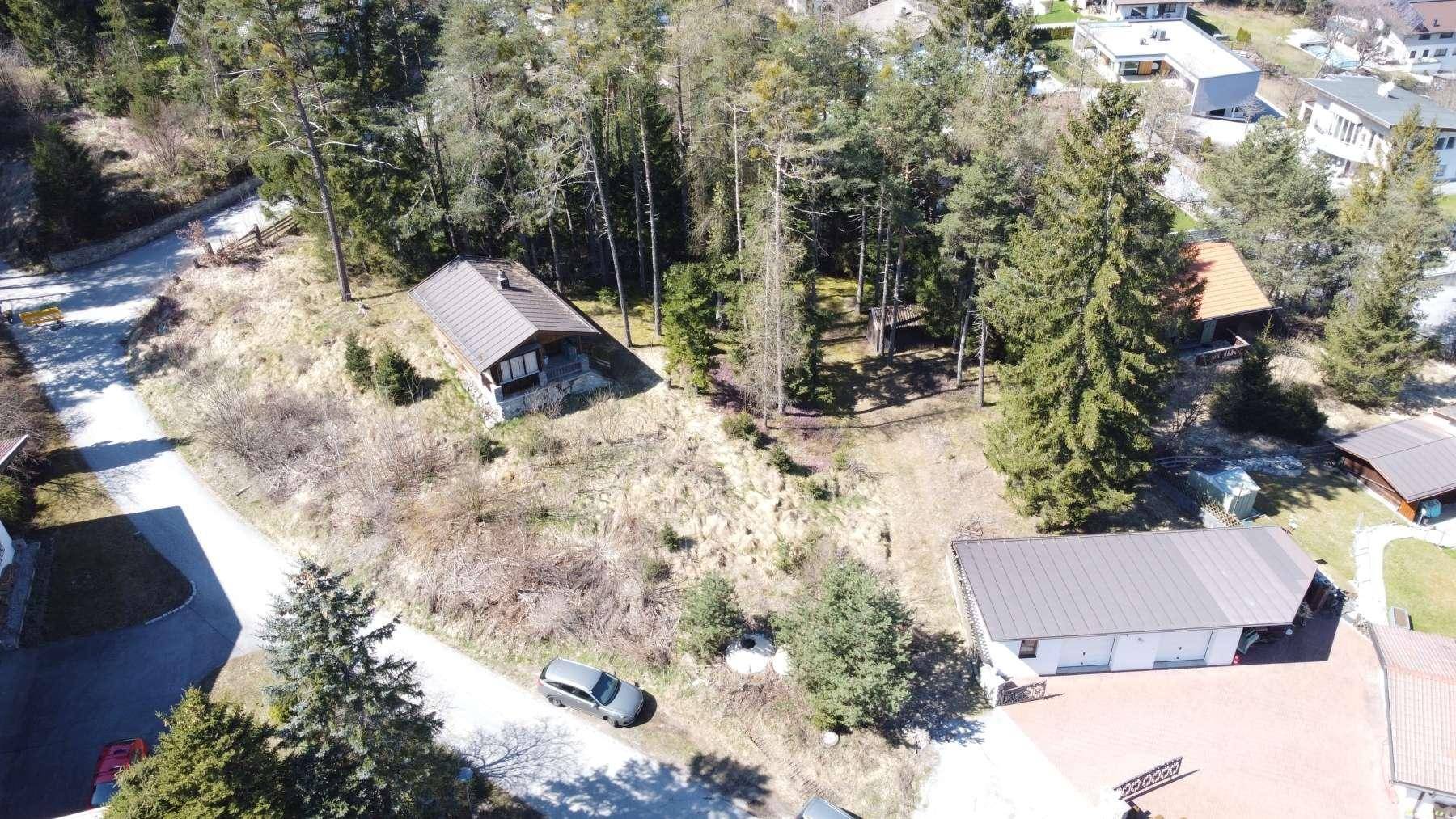 Luftaufnahme des Anwesens mit rustikalem Holzhaus, umgeben von Wald und weiteren Gebäuden in der Ferne.