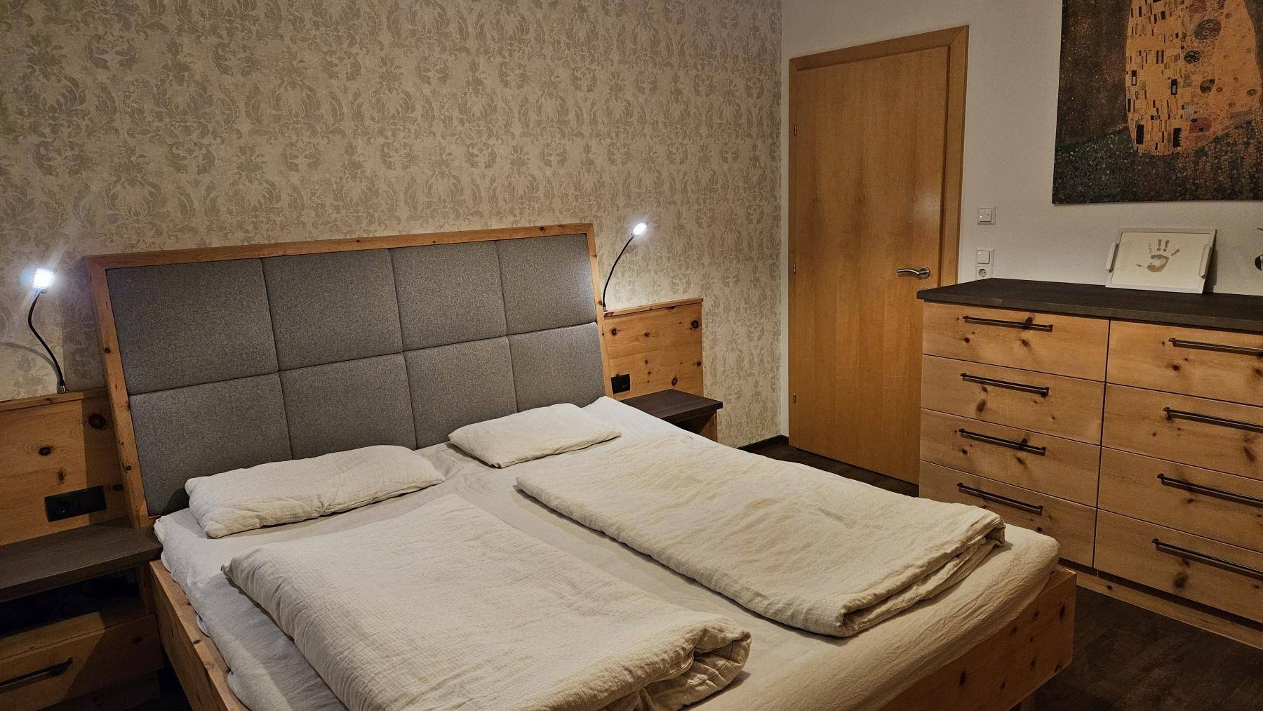 Schlafzimmer mit Holzbett, gepolstertem Kopfteil und passenden Holzmöbeln in gemütlicher Atmosphäre.