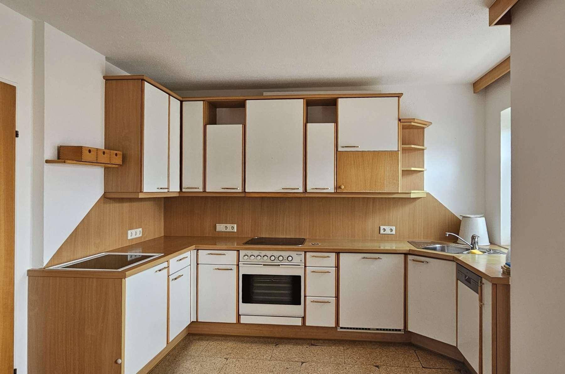 Funktionale Küche mit Holzschränken, weißen Fronten und integrierten Geräten, ideal für den täglichen Gebrauch.