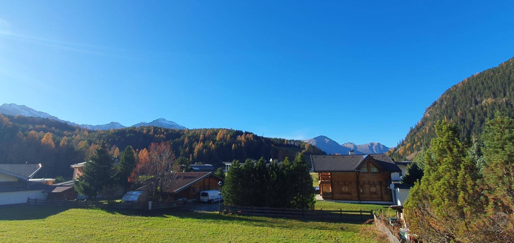 Panoramablick auf die umliegende Berglandschaft mit grünen Wiesen und vereinzelten Häusern.