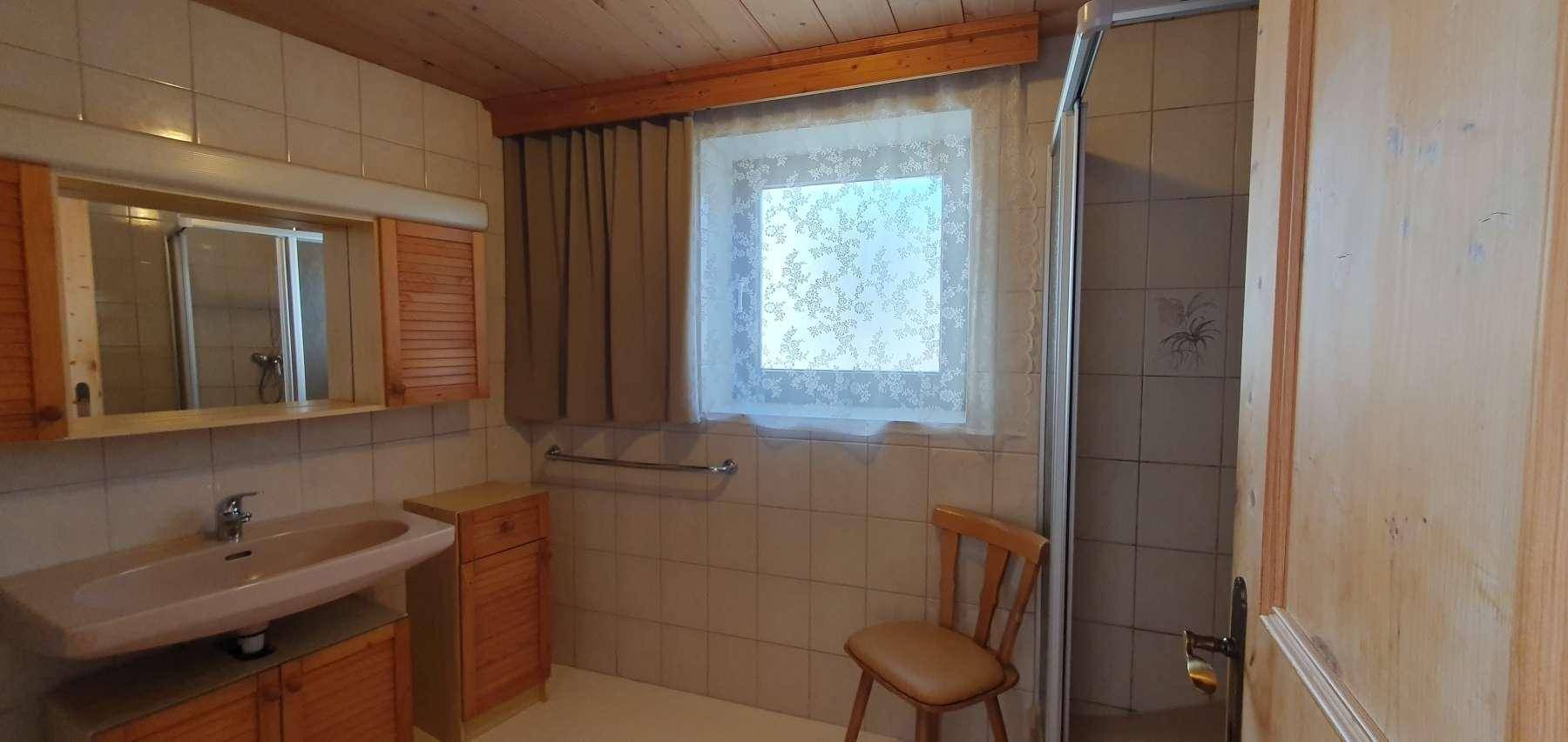 Funktionales Badezimmer mit hellen Fliesen, Dusche, Waschbecken und Fenster für natürliche Belüftung.