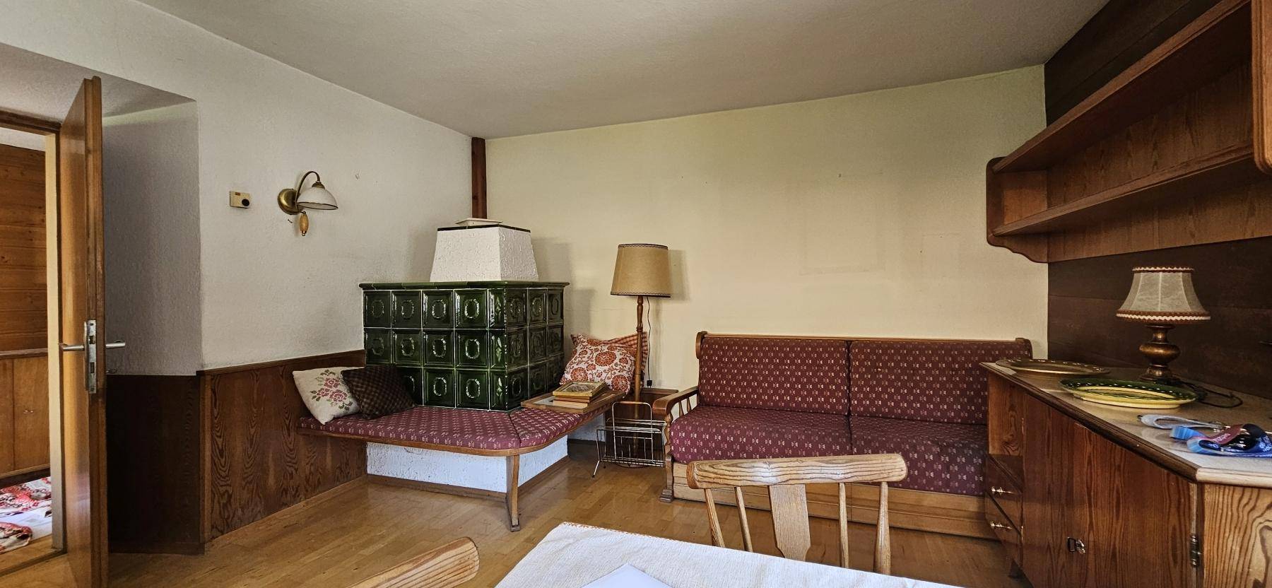 Gemütliches Wohnzimmer im alpinen Stil mit Kachelofen, Holzvertäfelung und traditionellen Möbeln.