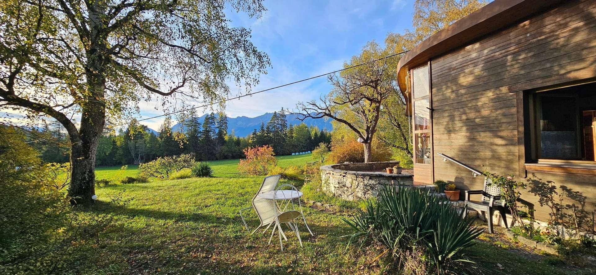 Gemütlicher Sitzbereich im Garten neben dem Haus mit Blick auf die umliegende Natur und Berge.
