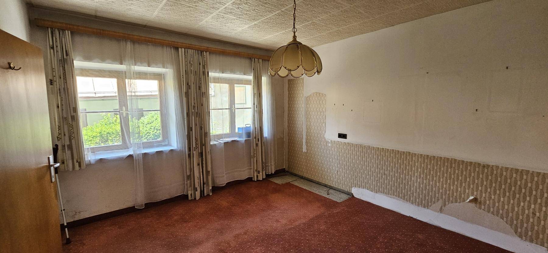 Schlafzimmer mit Teppichboden, Tapetenresten und Fenstern, bereit für eine Renovierung.