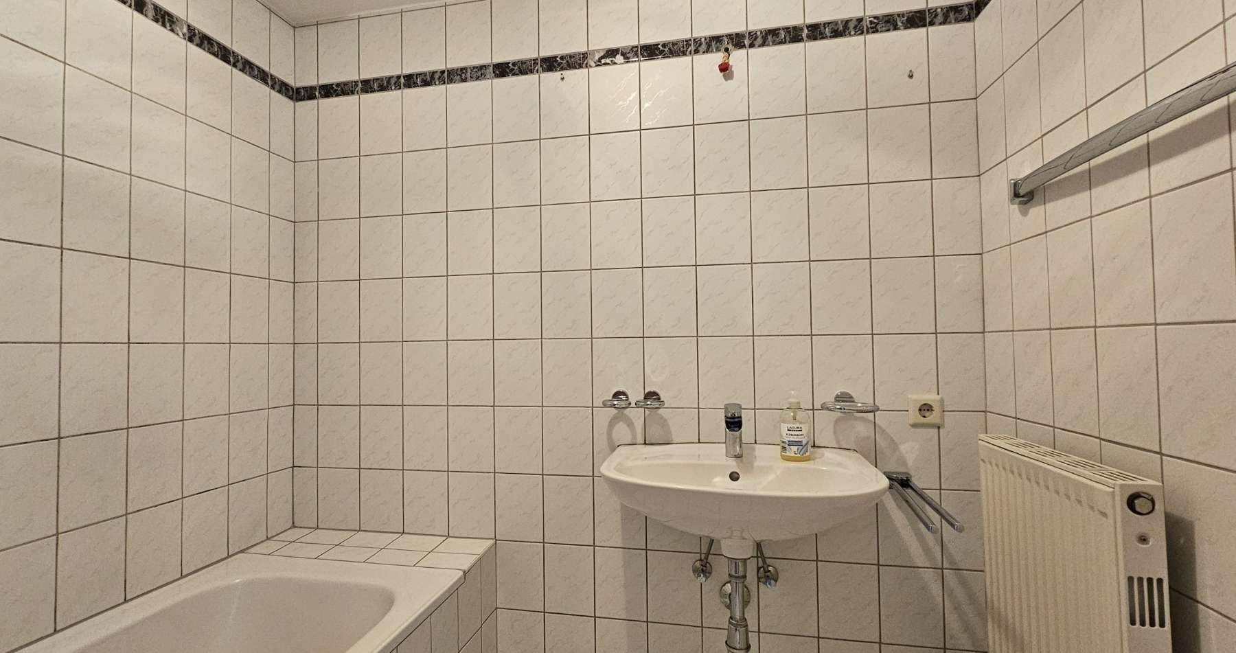 Badezimmer mit Badewanne, Waschbecken und Heizkörper, vollständig gefliest für eine pflegeleichte Umgebung.