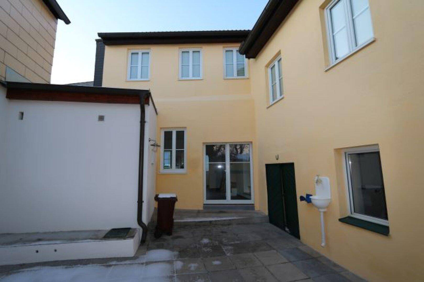 Außenansicht eines Gebäudes mit gepflastertem Hof und mehreren Fenstern.