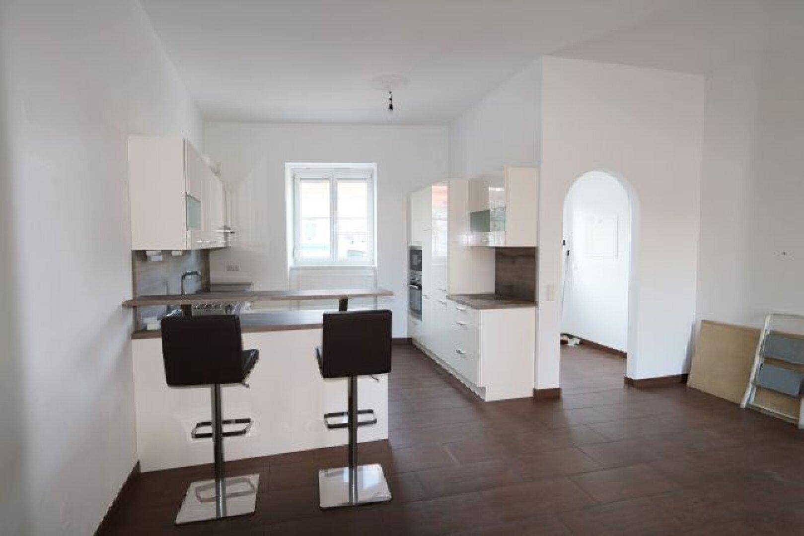 Moderne Küche mit weißer Einbauküche, Frühstücksbar und dunklem Boden.