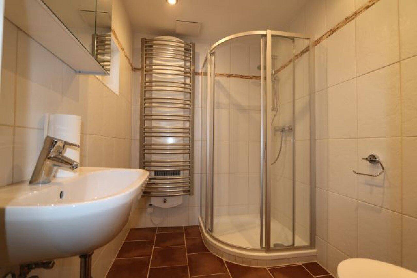 Funktionales Badezimmer mit Eckdusche, Waschbecken und beheiztem Handtuchhalter.