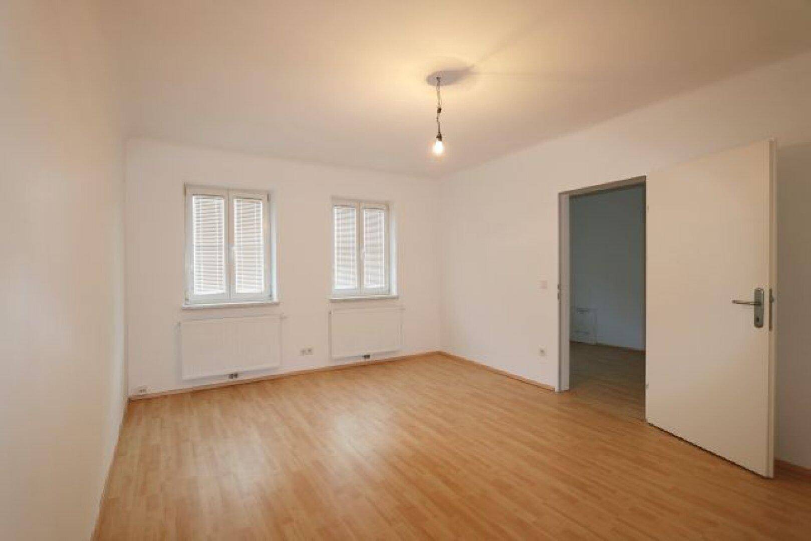 Geräumiges Schlafzimmer mit hellem Laminatboden und zwei Fenstern.