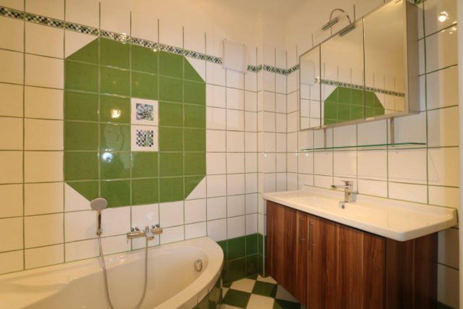 Badezimmer mit Badewanne, Waschbecken und auffälligen grün-weißen Fliesen.