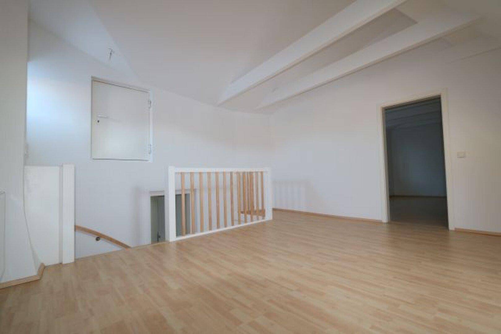 Heller Dachbodenbereich mit sichtbaren Deckenbalken und hellem Laminatboden.