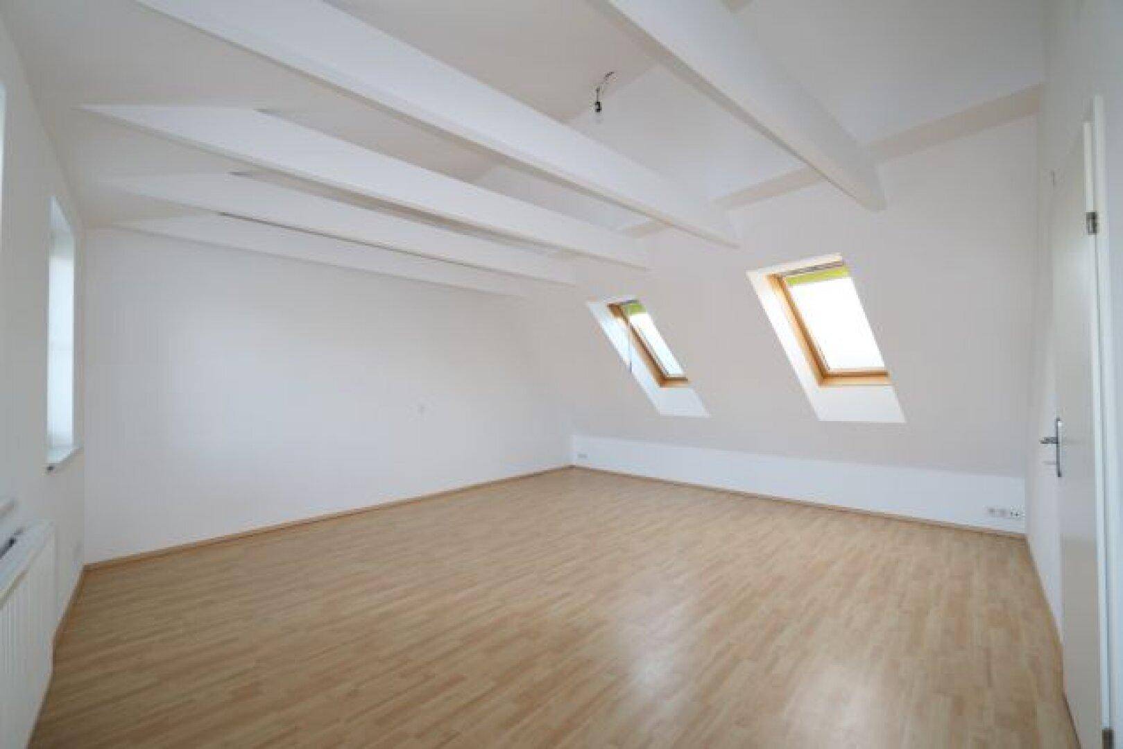 Dachgeschosszimmer mit schrägen Decken, sichtbaren Balken und zwei Dachfenstern.