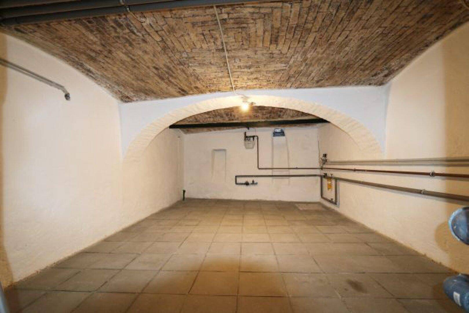 Kellerraum mit gemauertem Gewölbe, sichtbaren Rohren und Fliesenboden.