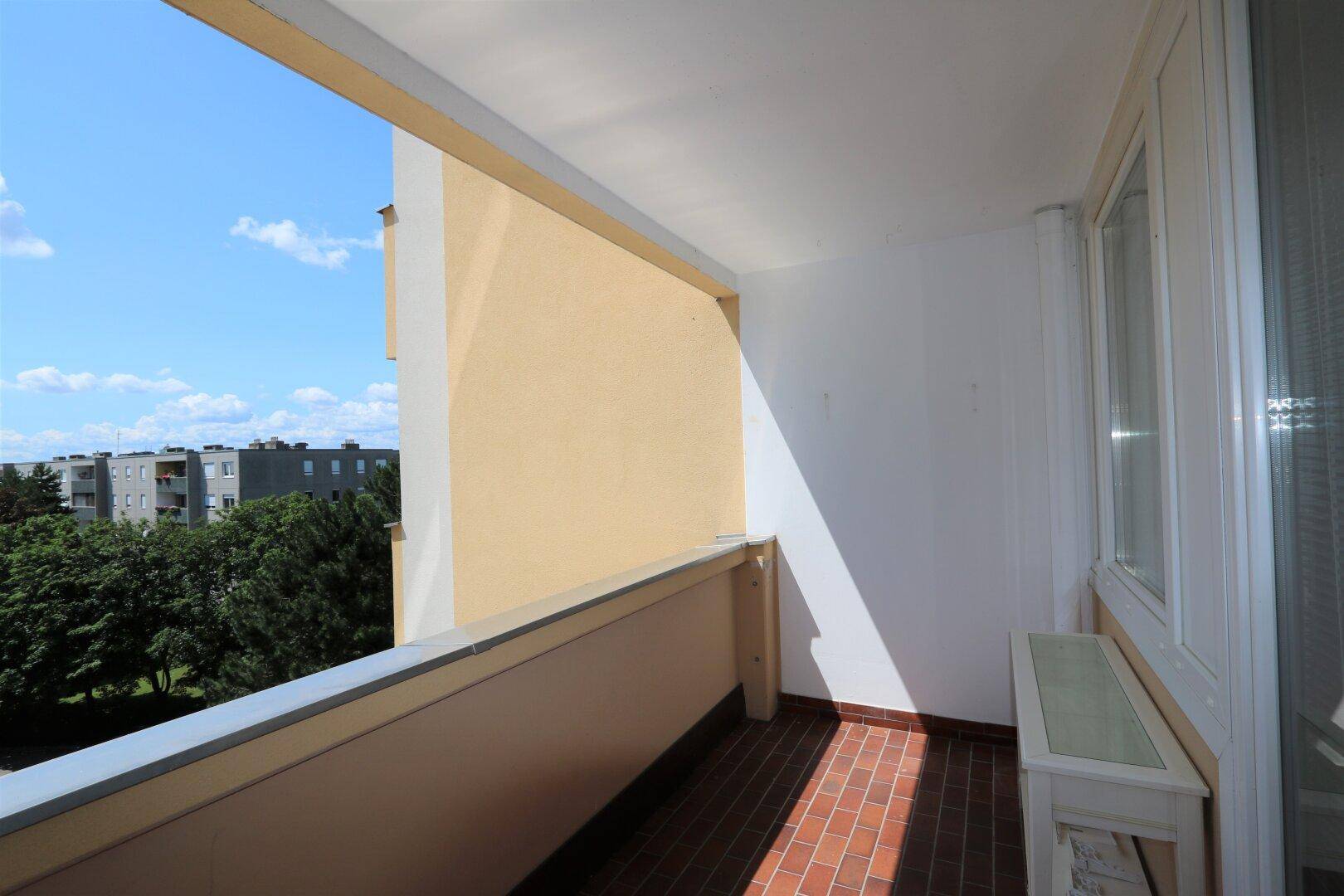 Heller Balkon mit Fliesenboden und einer kleinen Bank, bietet einen Blick auf die Umgebung.