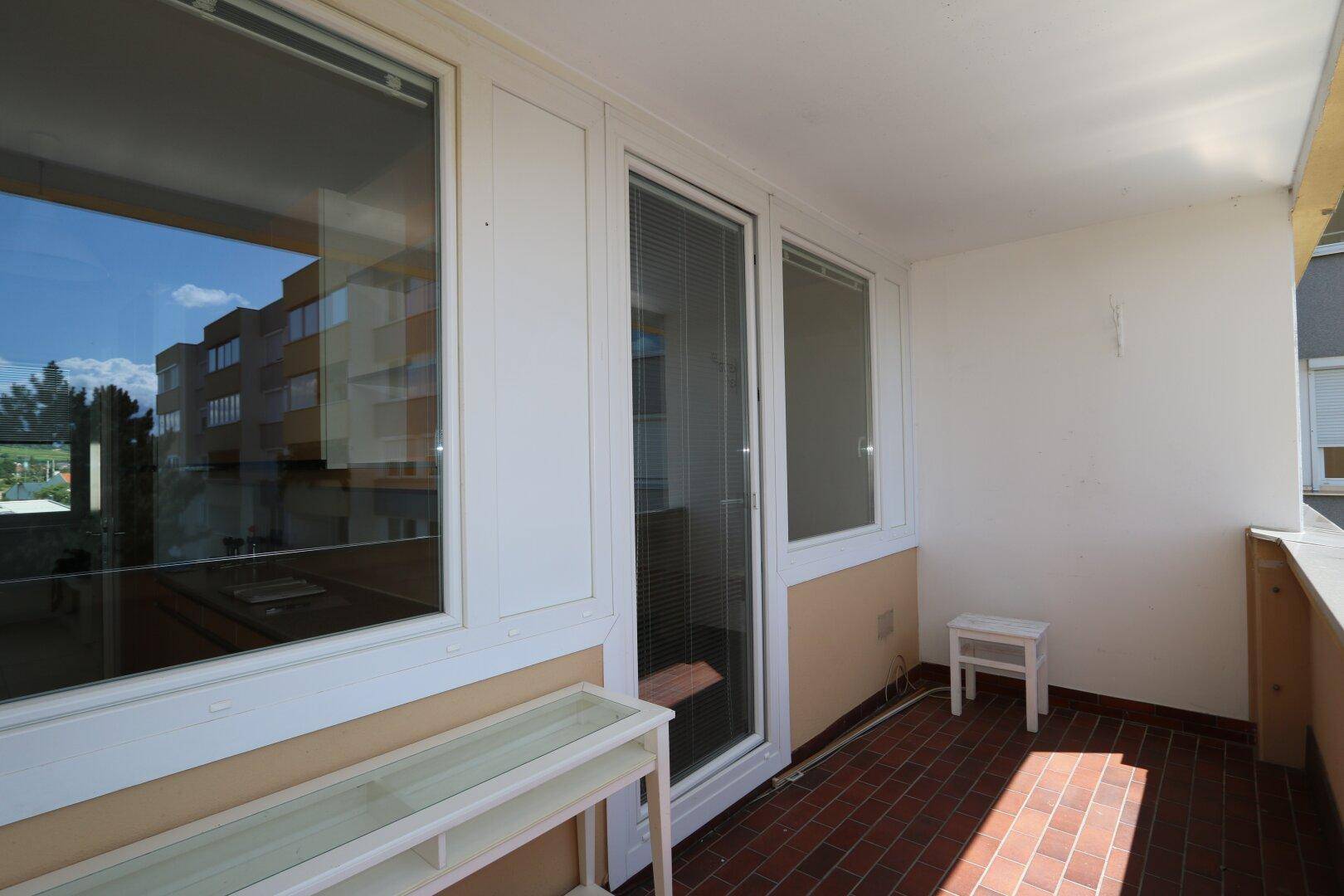 Balkon mit Fliesenboden und Zugangstür zum Innenbereich, umgeben von hellen Wänden.