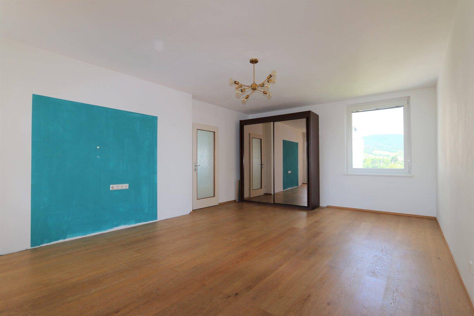 Geräumiges Zimmer mit Holzboden, Spiegelschrank und Fenster mit Blick ins Grüne.