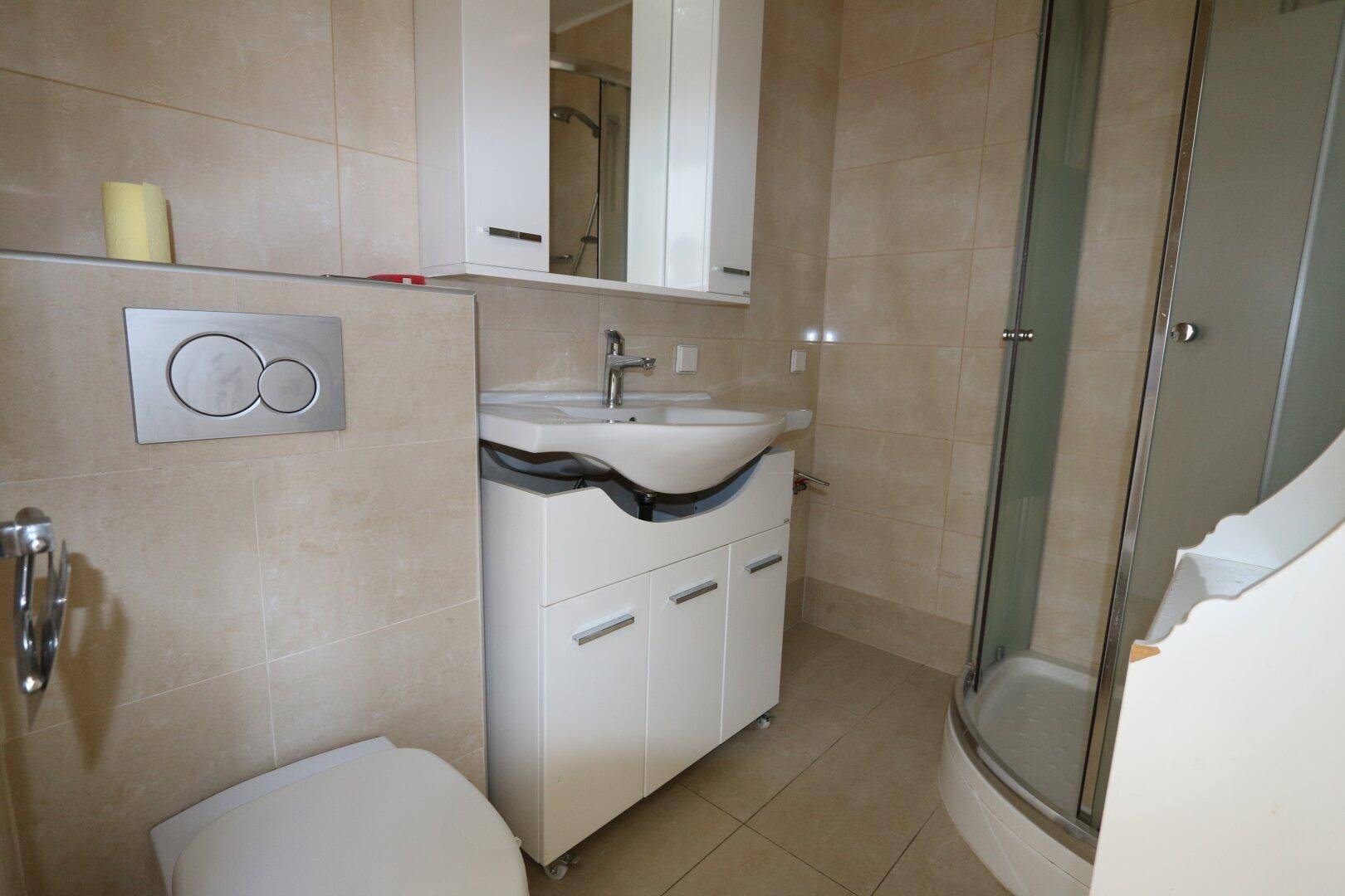 Modern gefliestes Badezimmer mit Waschtisch, Toilette und einer Duschkabine in der Ecke.