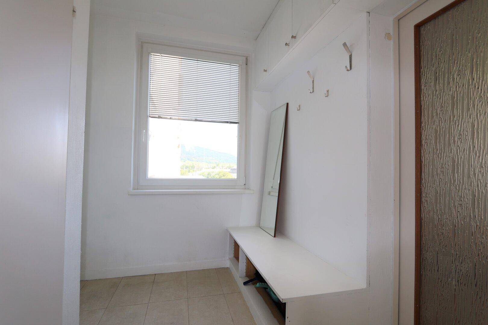 Heller Flur mit Fliesenboden, Fenster und einer Garderobenbank mit Haken.