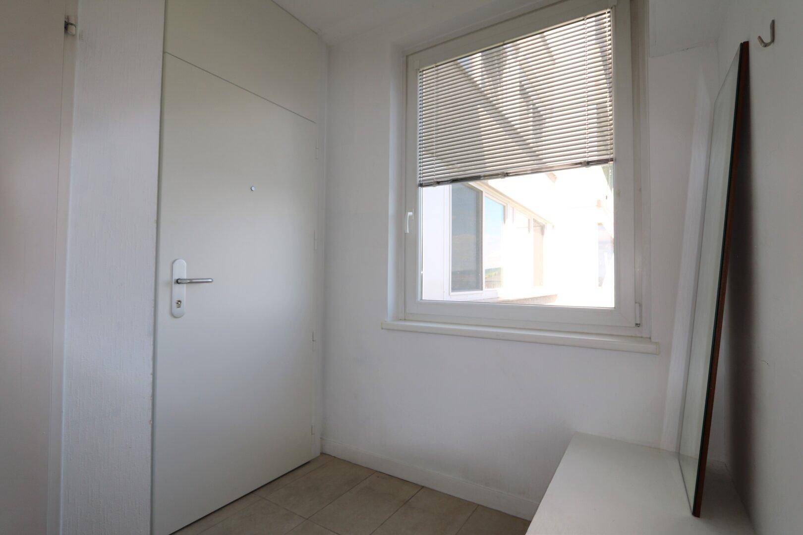 Eingangsbereich mit weißer Tür, Fenster und Fliesenboden, bietet einen hellen Empfang.