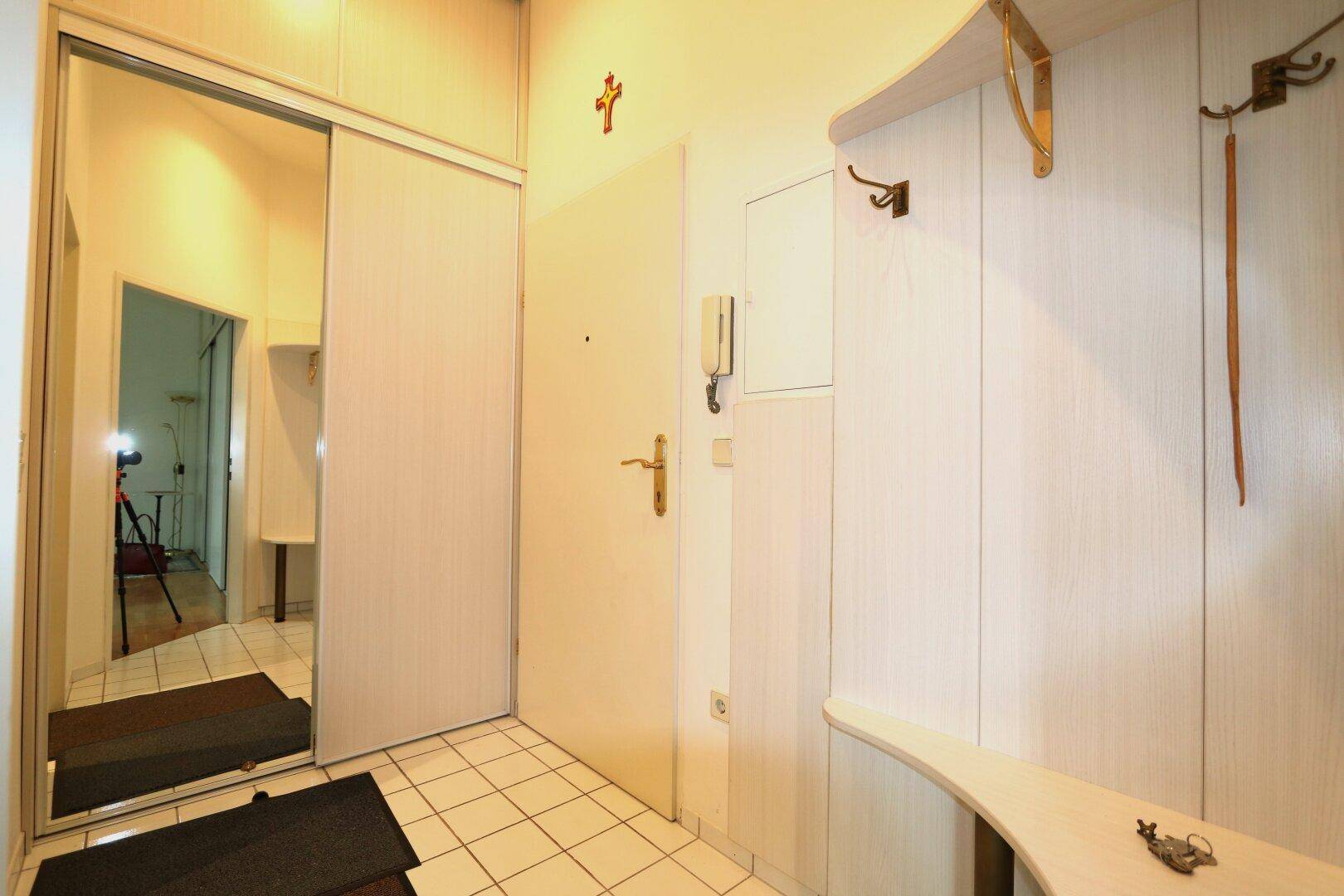 Heller Eingangsbereich mit Fliesenboden, Garderobe und großem Spiegelschrank, der den Raum erweitert.
