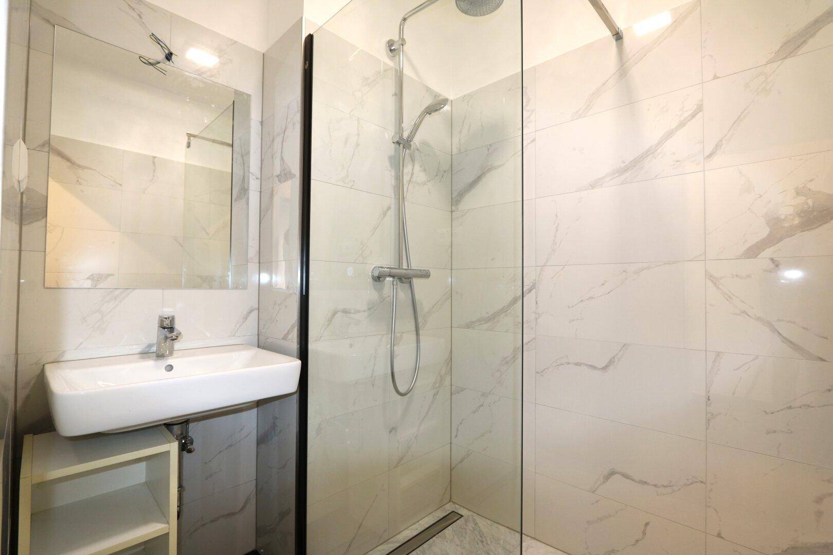 Modernes Badezimmer mit begehbarer Dusche, Einzelwaschbecken und hellen Marmorfliesen.
