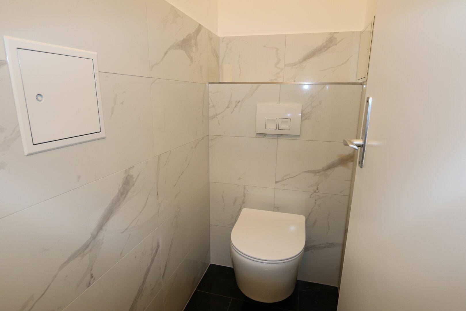 Separates WC mit wandhängender Toilette und modernen Fliesen in Marmoroptik.