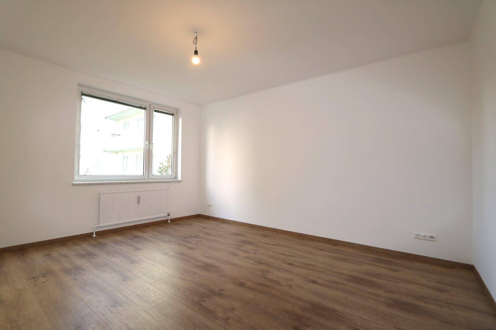 Geräumiger, heller Raum mit Laminatboden und großen Fenstern, ideal als Wohn- oder Schlafzimmer.