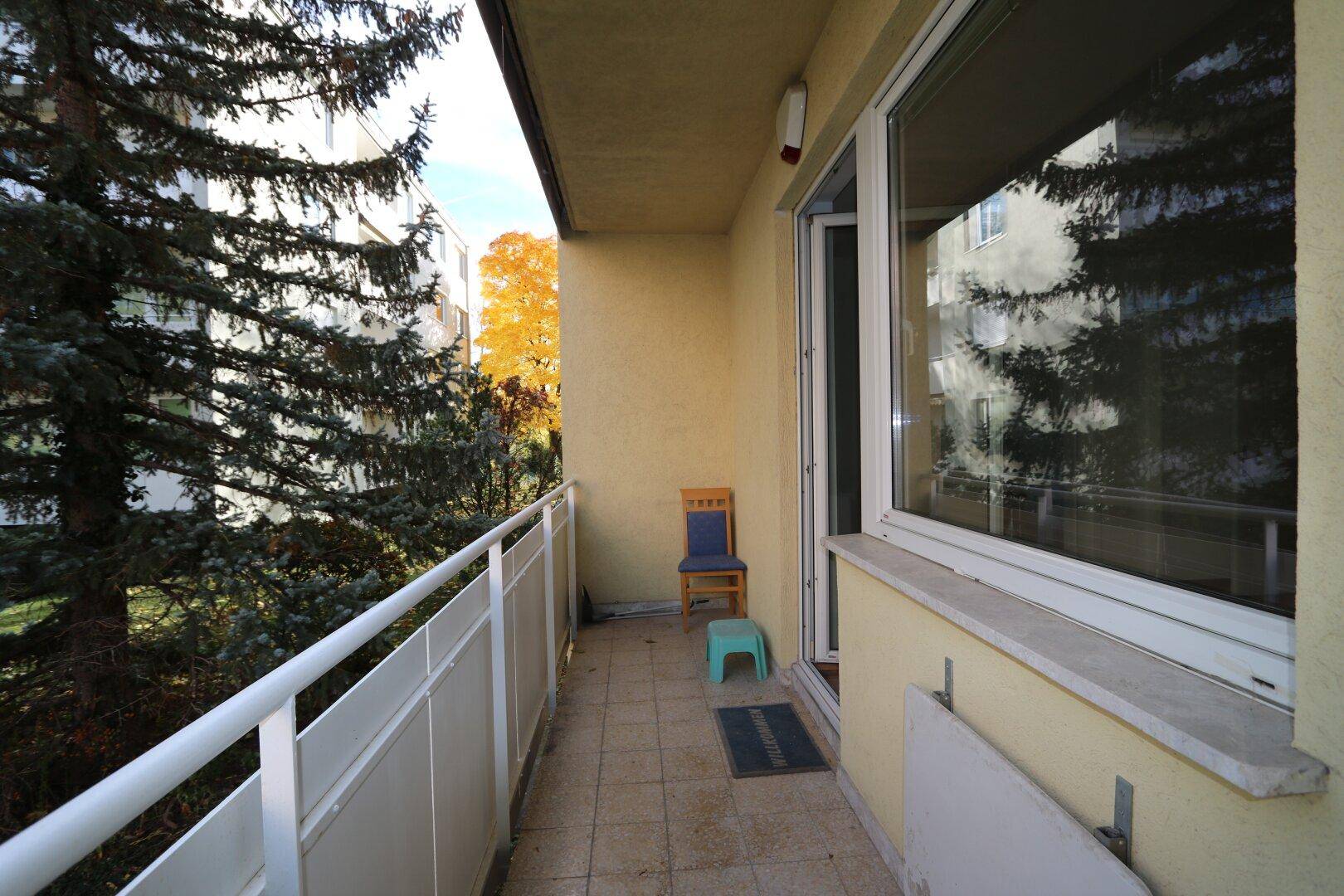 Schmaler Balkon mit Fliesenboden, weißem Geländer und Blick ins Grüne.