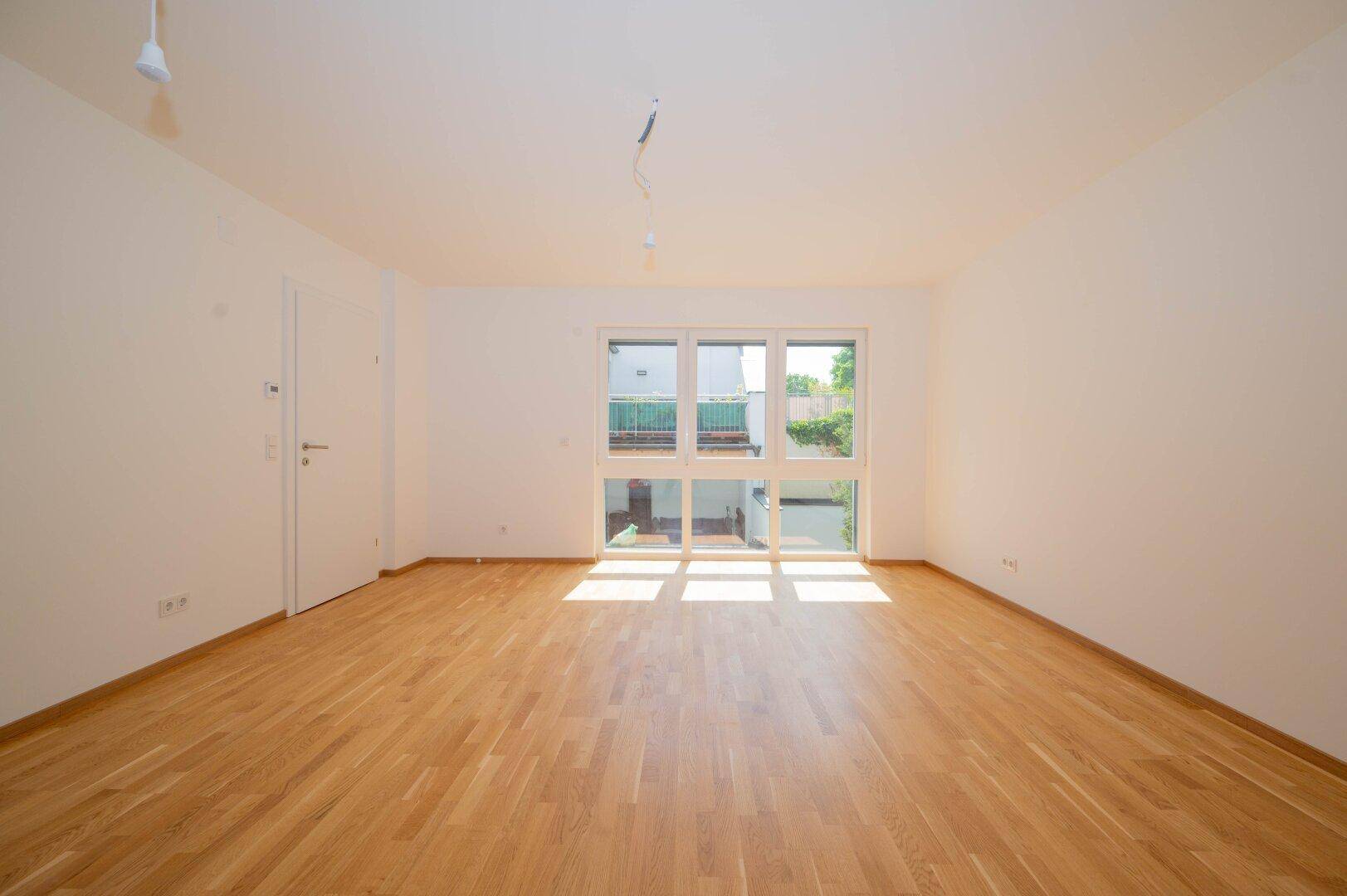 Heller Raum mit Holzboden und großen Fenstern, die einen Blick auf den Innenhof bieten.