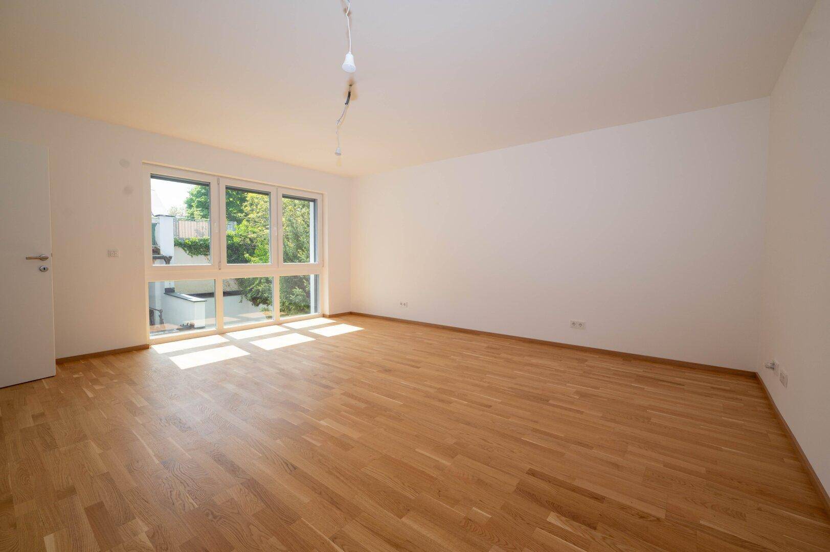 Helles Zimmer mit Holzboden und großen Fenstern, die viel Tageslicht hereinlassen.