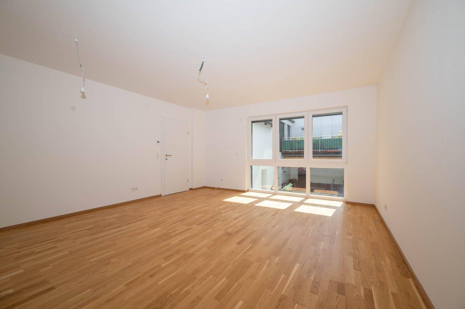 Heller Raum mit Holzboden und großen Fenstern, die einen Blick auf den Innenhof bieten.
