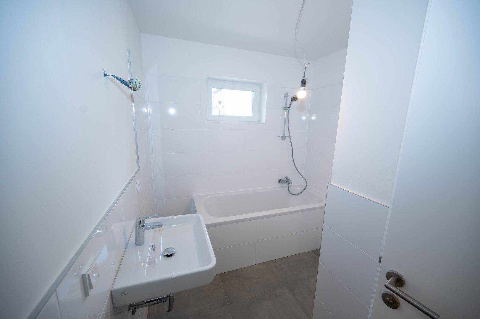 Modernes Badezimmer mit weißen Fliesen, Badewanne und einem kleinen Fenster für Tageslicht.
