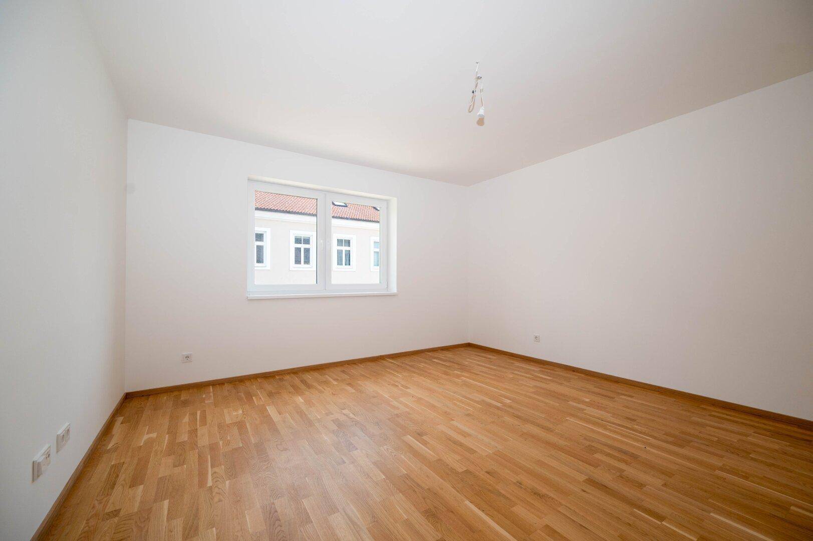 Leeres Zimmer mit hellem Parkettboden und weiß gestrichenen Wänden, bereit zur Einrichtung.