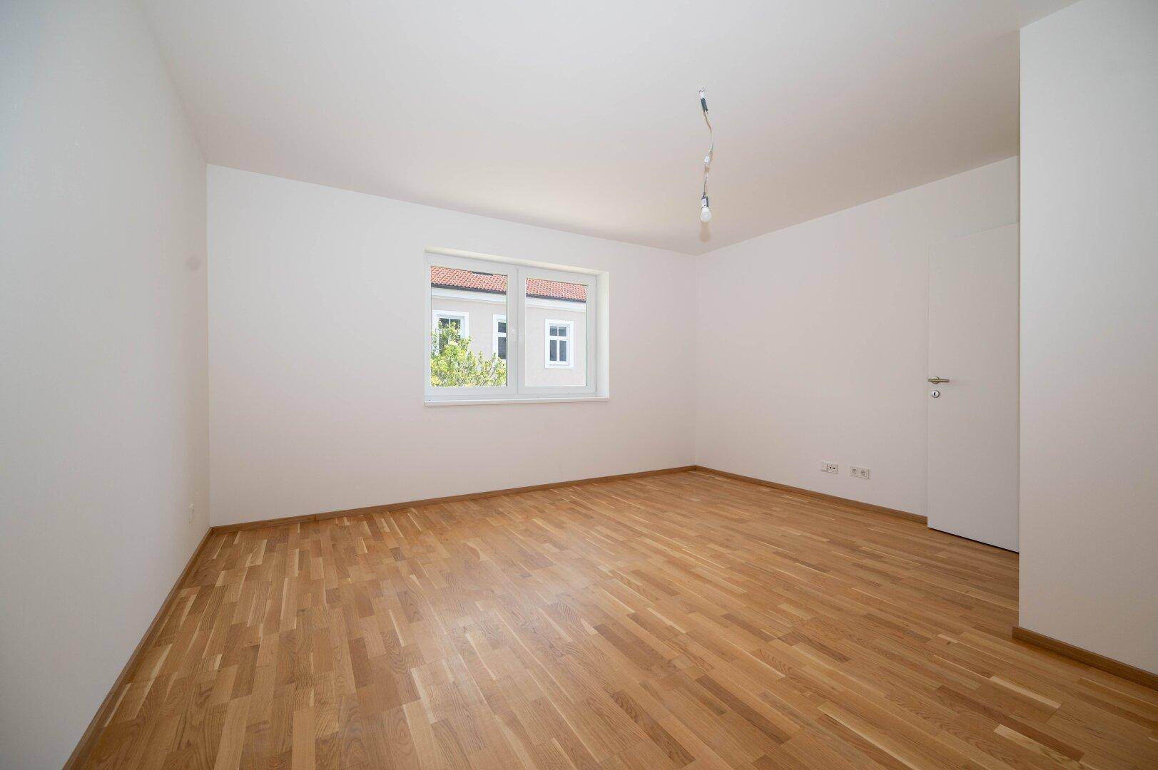 Geräumiges Zimmer mit Parkettboden und einem Fenster mit Blick auf die Nachbarschaft.