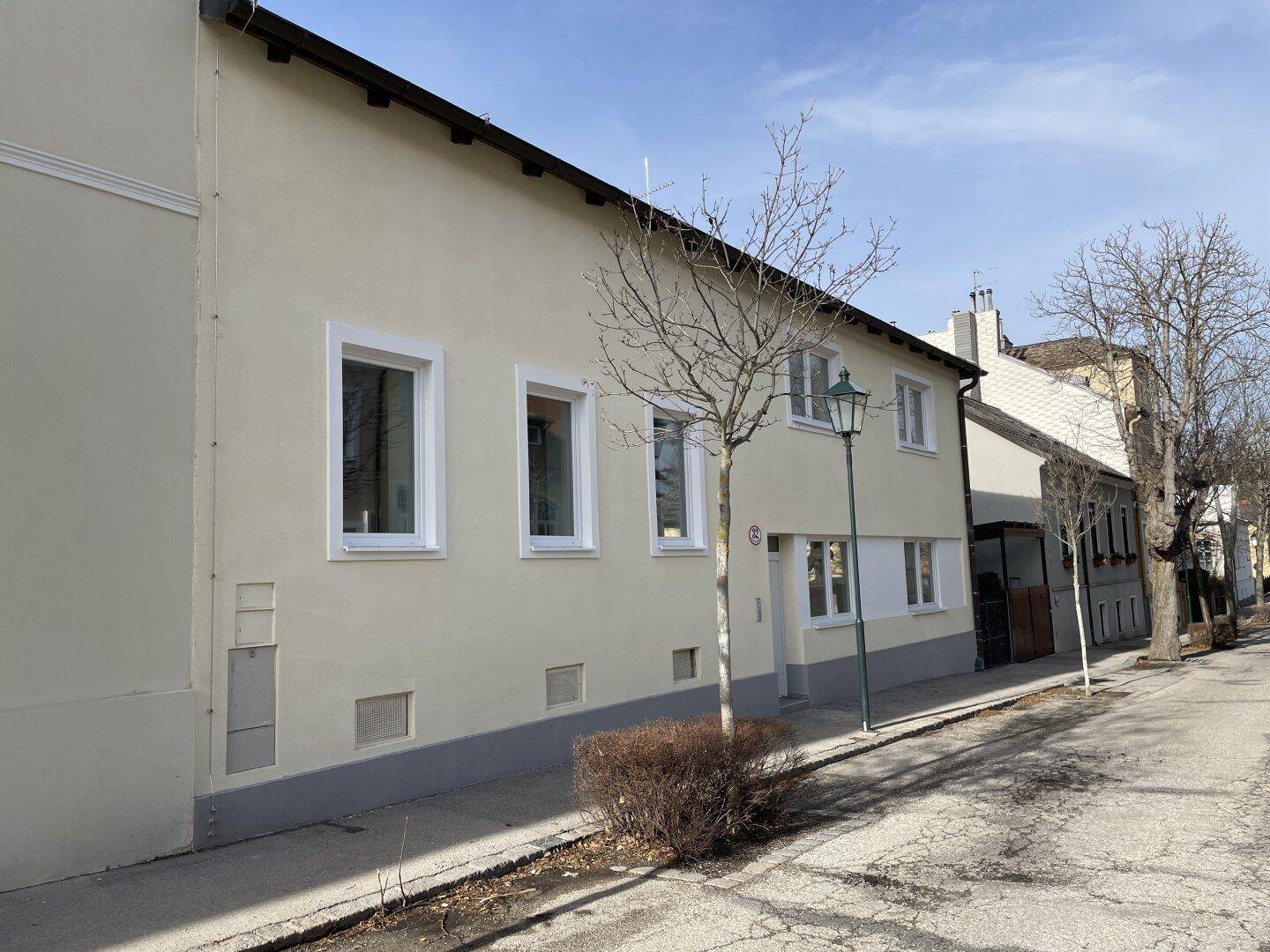 Ansicht der Gebäudefassade von der Straße aus mit beiger Putzfassade und weißen Fenstern.